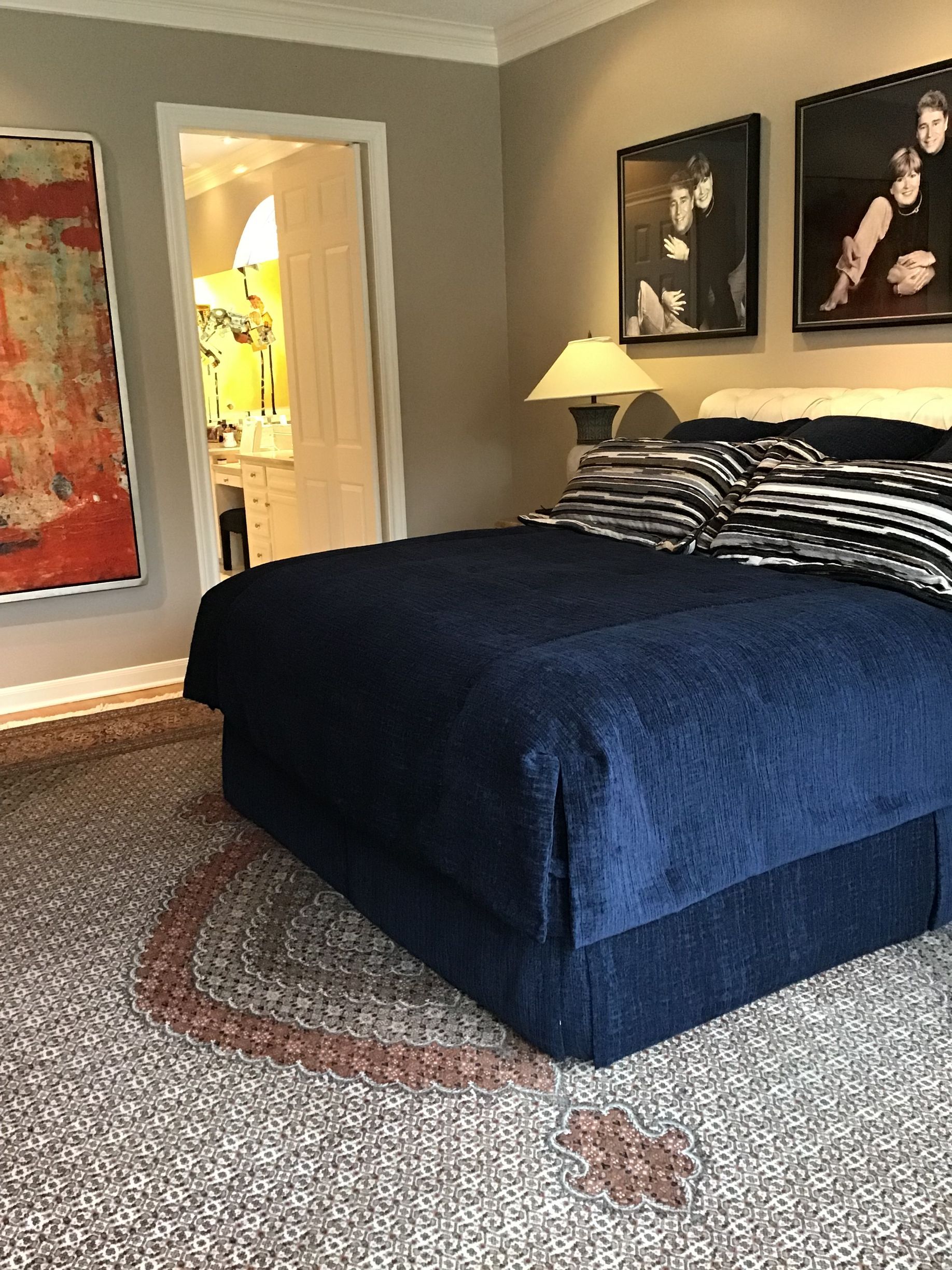 A bedroom with a navy blue bed, a textured gray rug, a floor lamp, and framed black-and-white photos on a neutral wall.