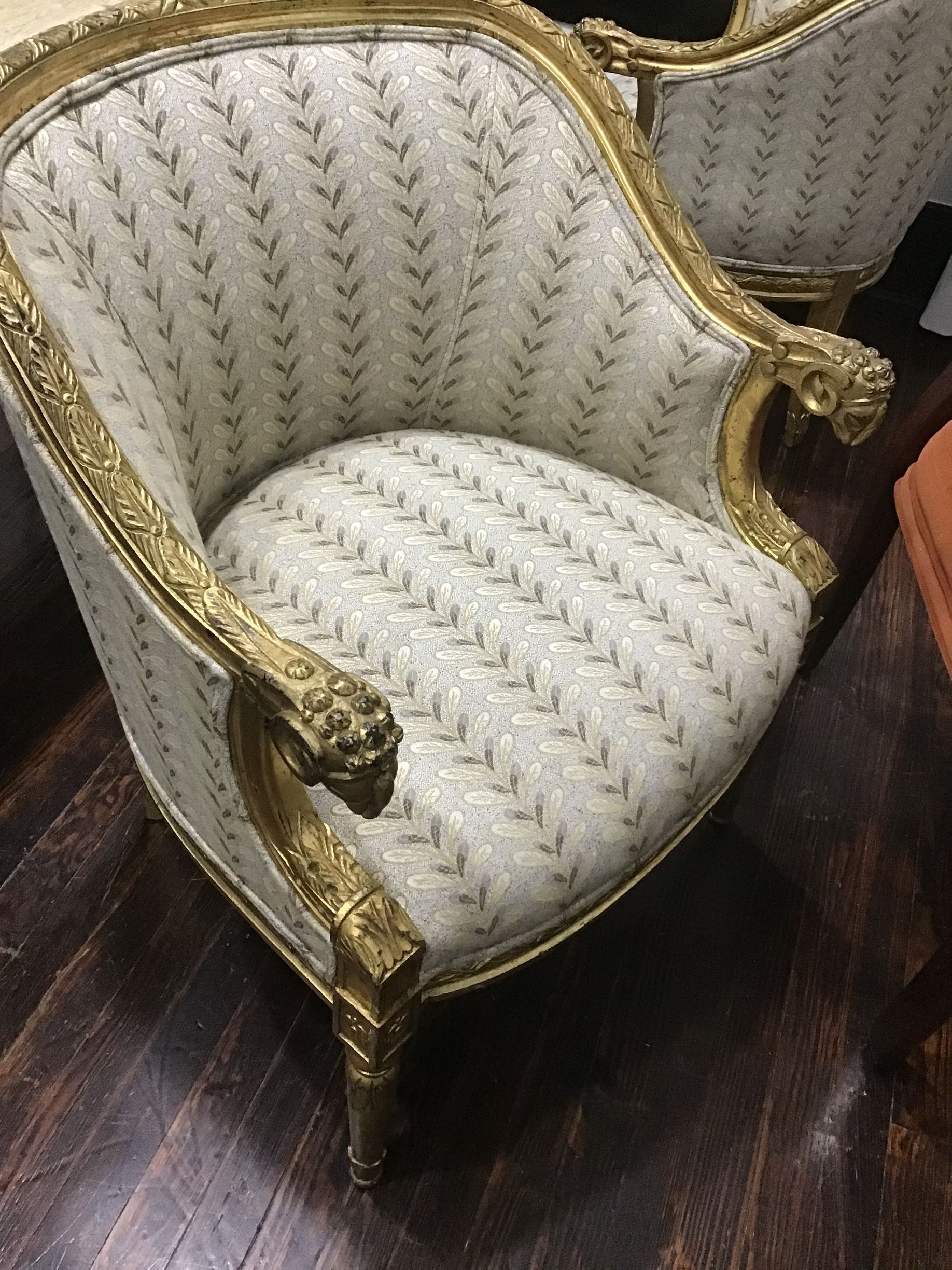 An ornate, gold-framed bergère chair upholstered in white fabric with a repeating vertical floral vine pattern.