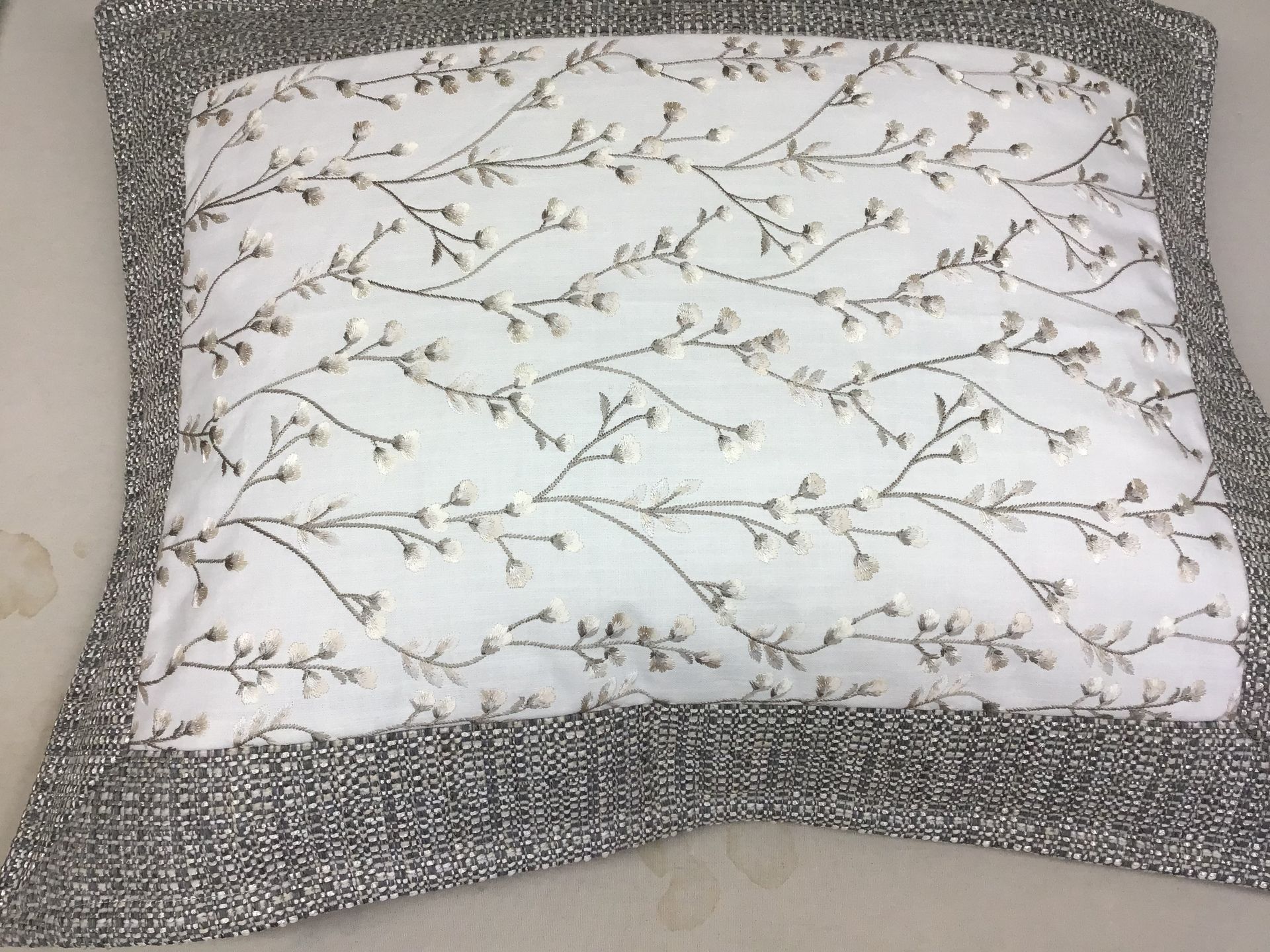 A square decorative pillow featuring a white center with a delicate brown branch pattern and a dark gray textured border.
