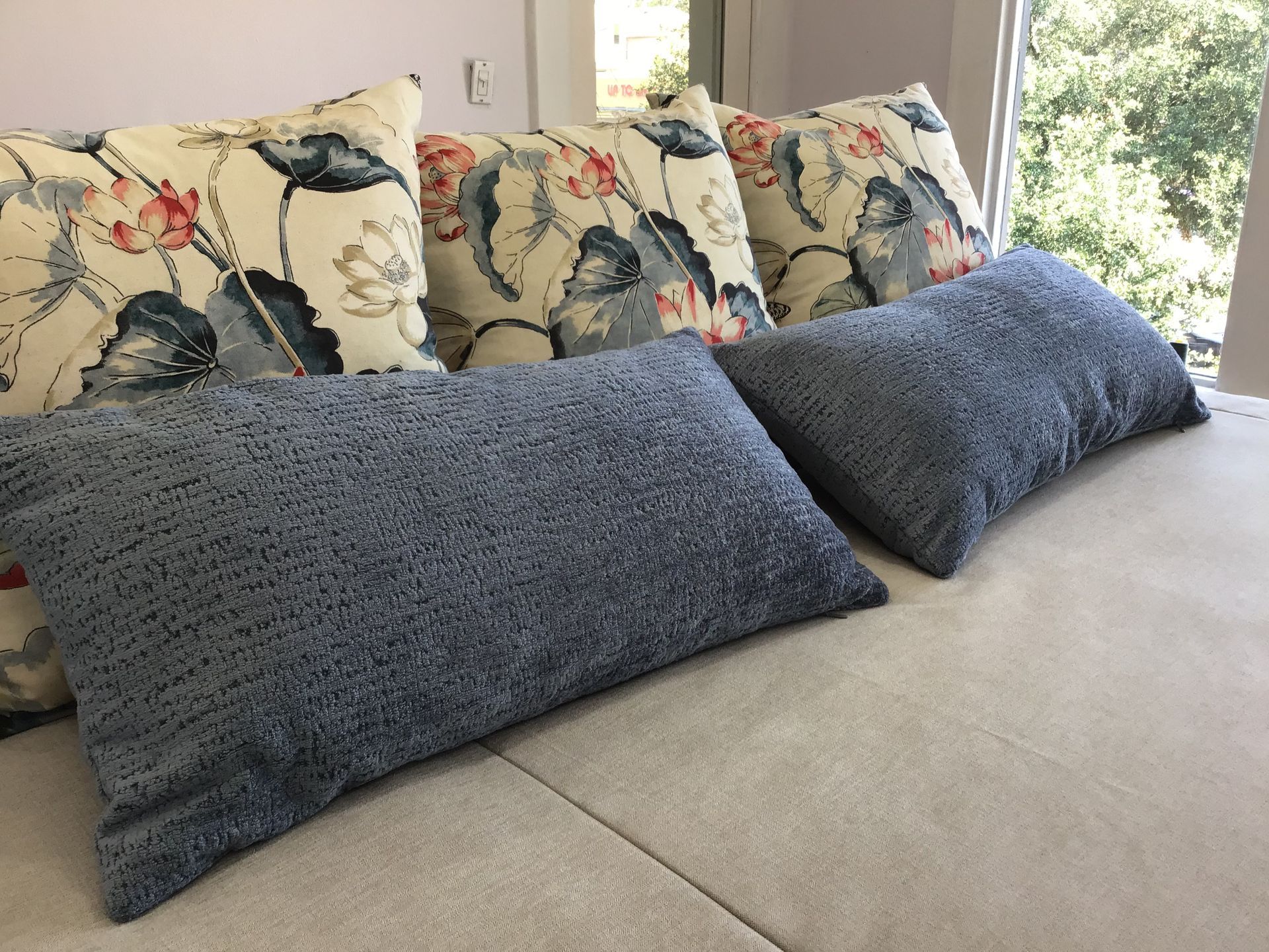 Two blue textured rectangular pillows in front of three square pillows with a cream, floral, and leaf print.