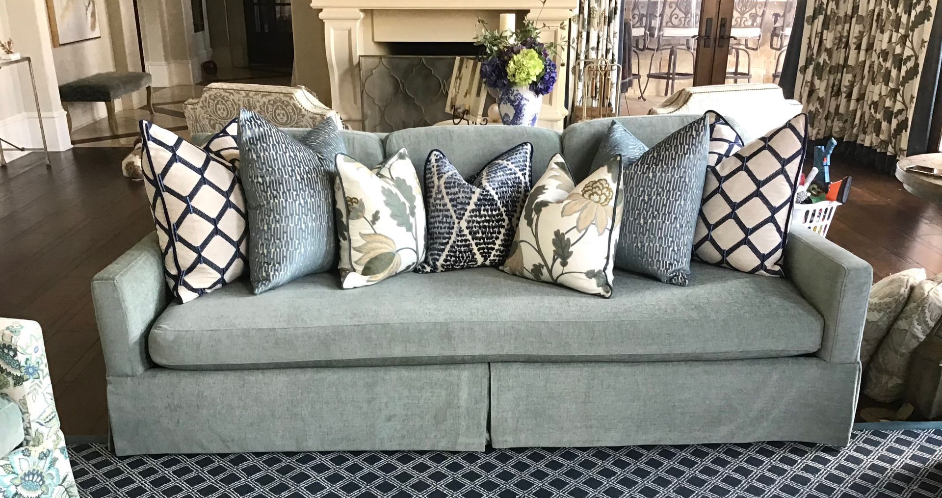 A light blue sofa with a skirted base, decorated with assorted patterned throw pillows in a room with hardwood floors.