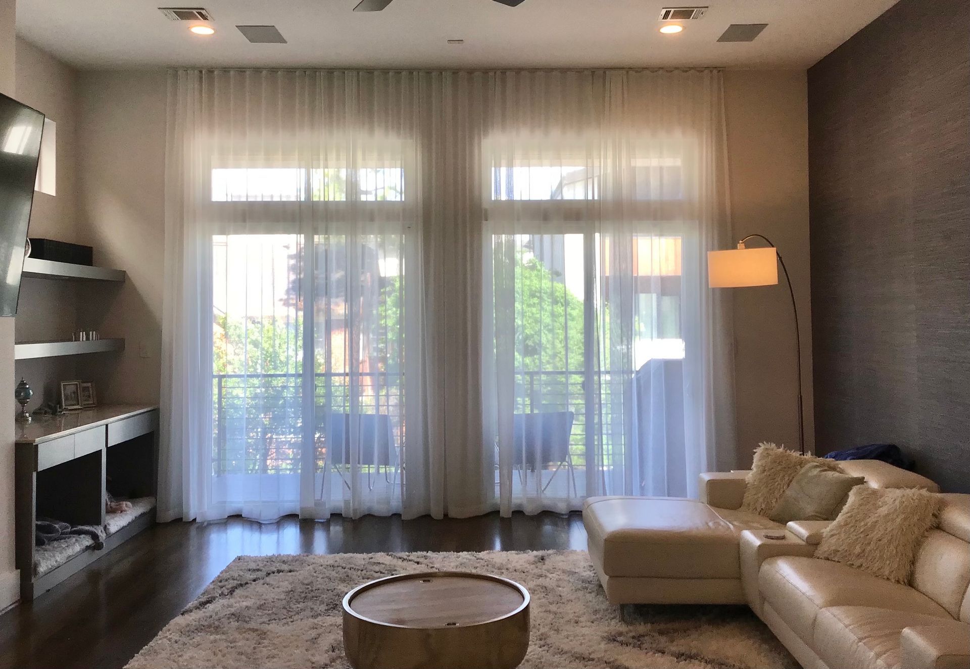 A modern living room with a white leather sectional, a round coffee table, sheer white curtains, and a dark accent wall.