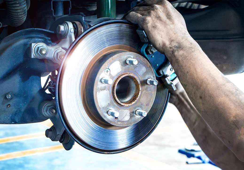 Mechanic working on car brake disc and caliper, focusing on repairs.
