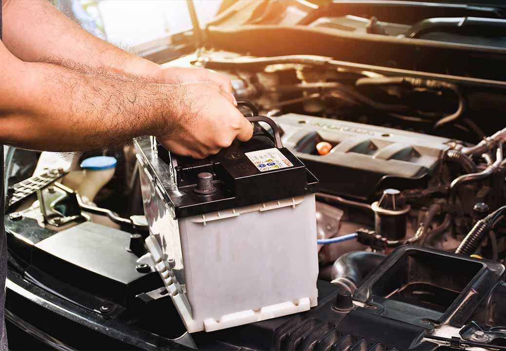 Person holding a car battery, engine bay visible.