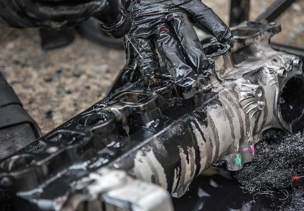 Gloved hands cleaning a metal object with black lubricant; close-up shot.