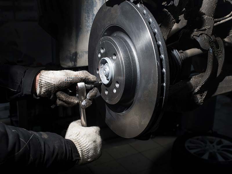 Mechanic using a hammer on a car's brake disc in a garage.