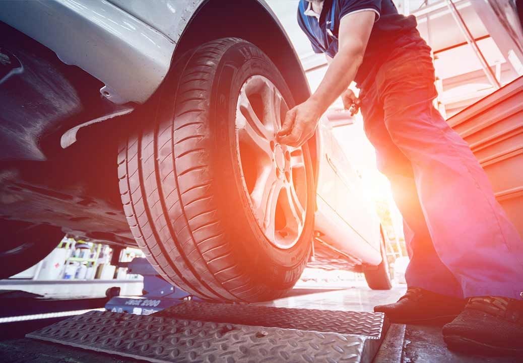 Mechanic changing a tire on a car lifted in a shop. Sunlight flares.