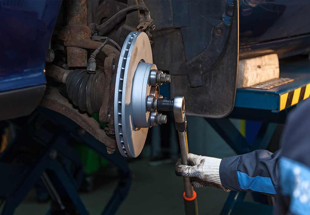 Mechanic working on car brake system with a wrench, focusing on the rotor, in a garage setting.