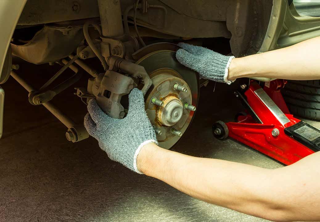Mechanic working on car brake system with a wrench, focusing on the rotor, in a repair shop.