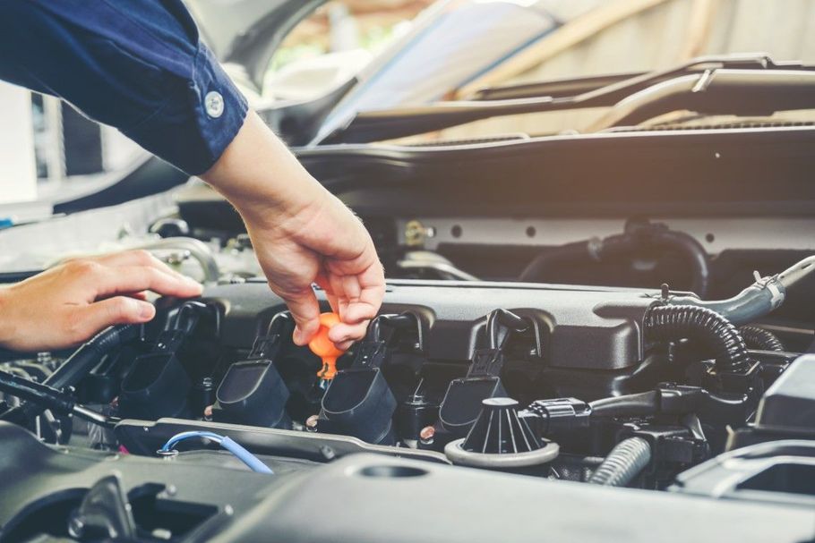 Mechanic checking car engine with an orange dipstick under the hood