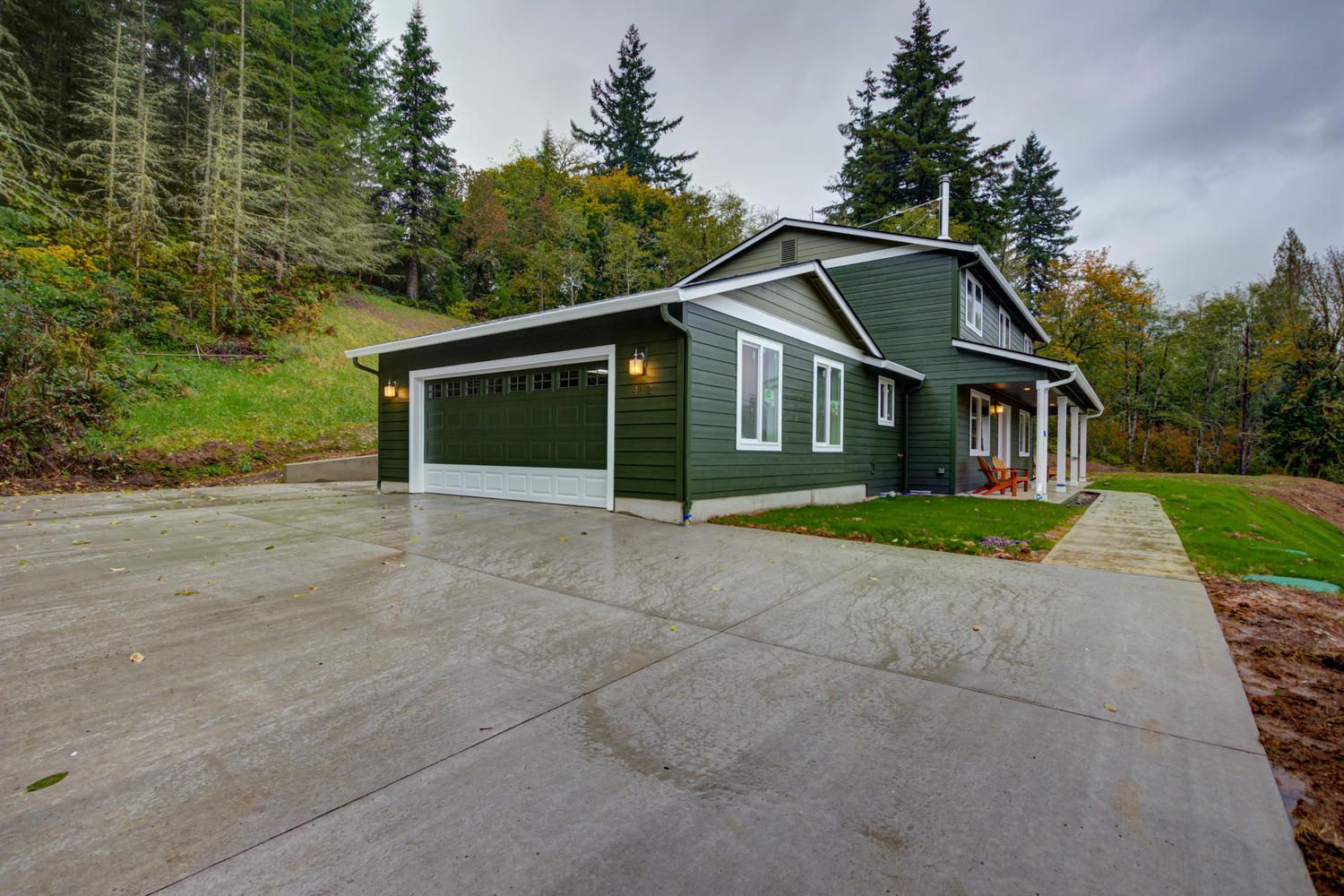 A green house with a garage and a driveway in front of it.