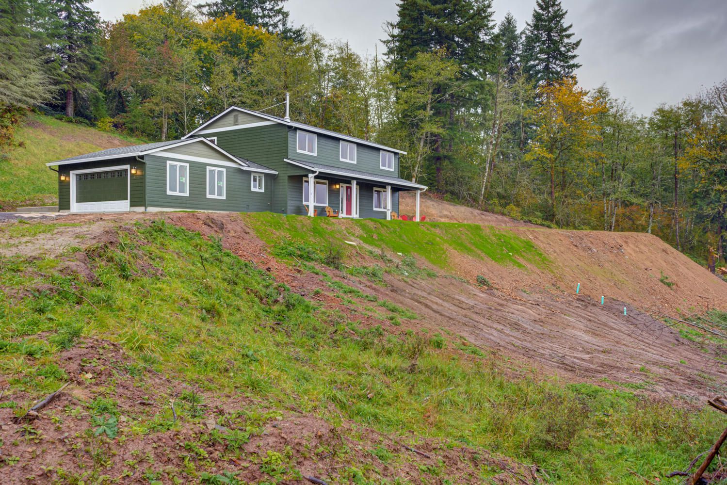 A green house is sitting on top of a hill surrounded by trees.