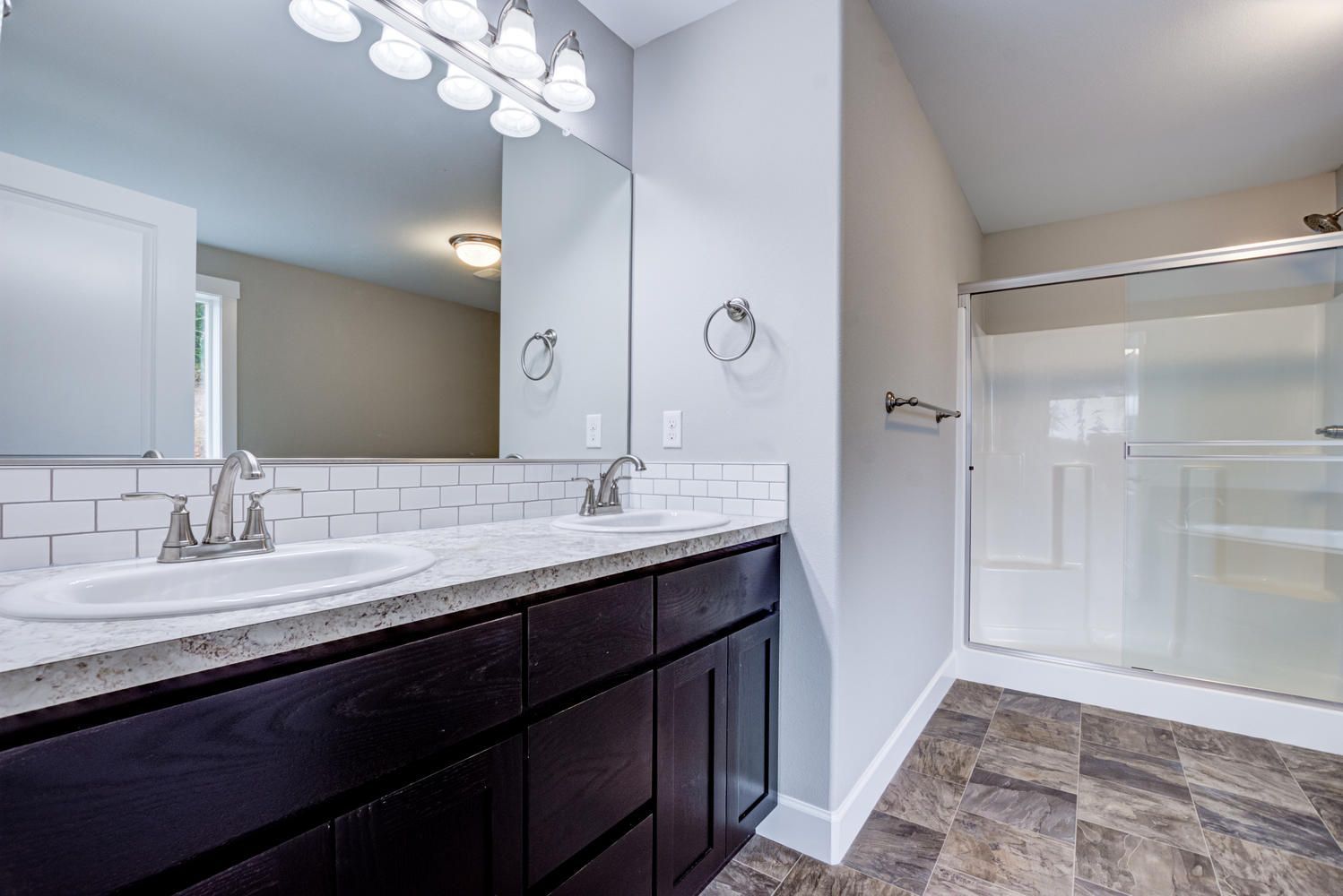 A bathroom with two sinks , a mirror and a walk in shower.