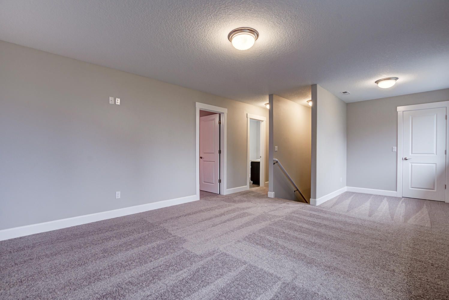 An empty basement with a staircase and a carpeted floor.