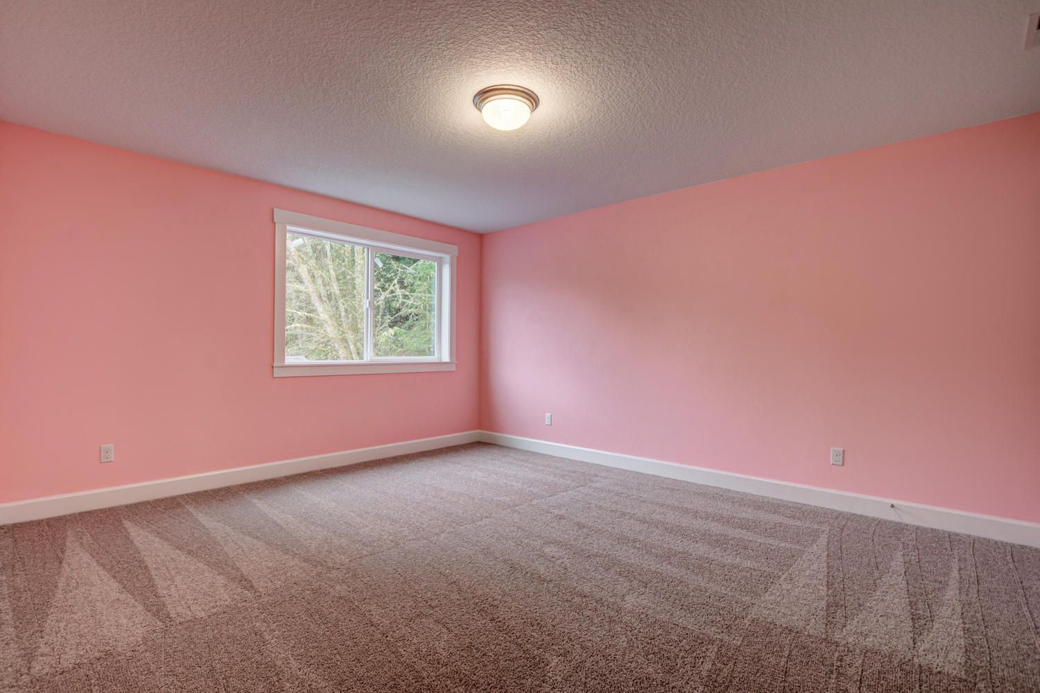 An empty bedroom with pink walls and a carpeted floor.