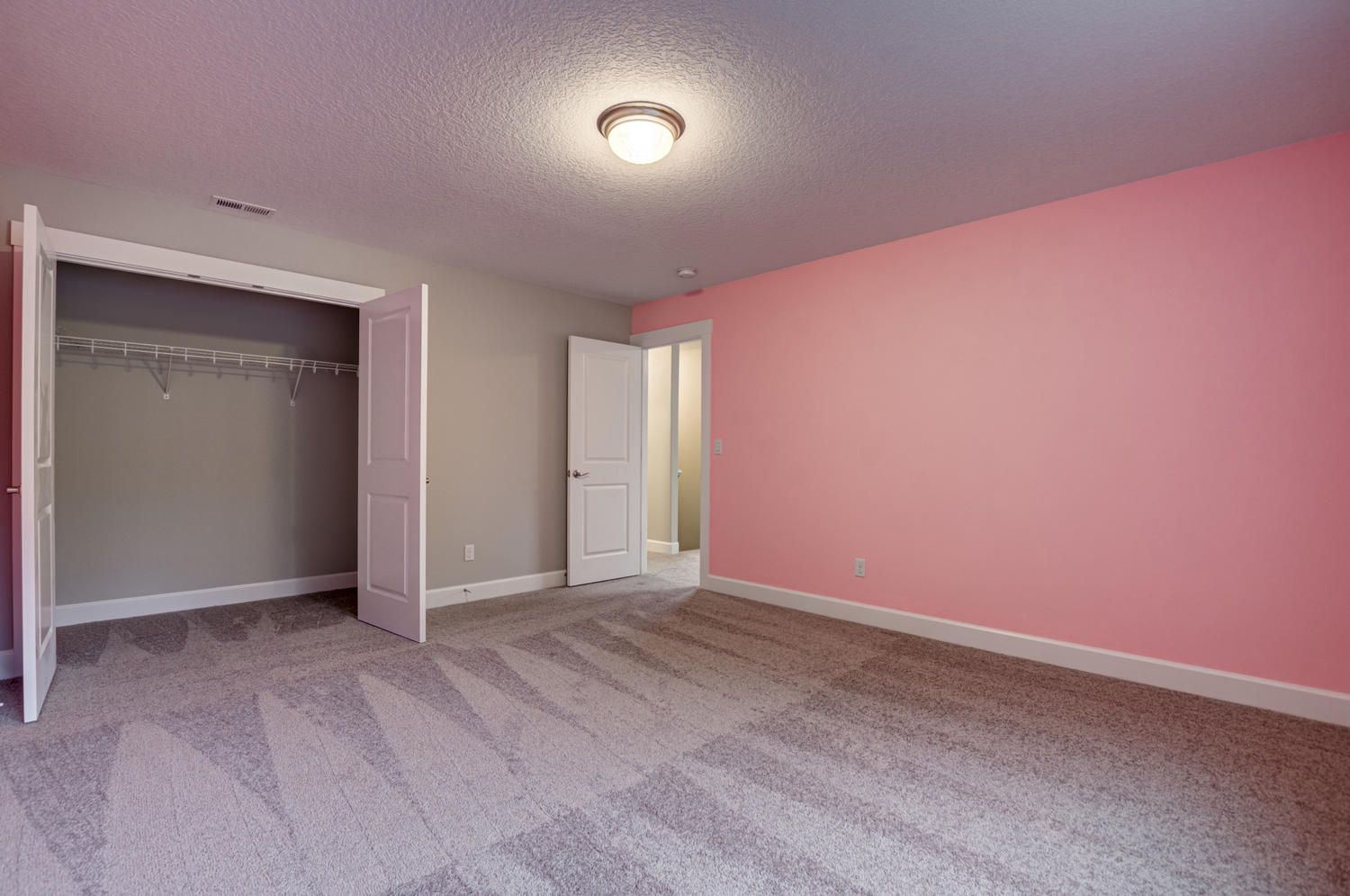 An empty bedroom with pink walls and a closet.