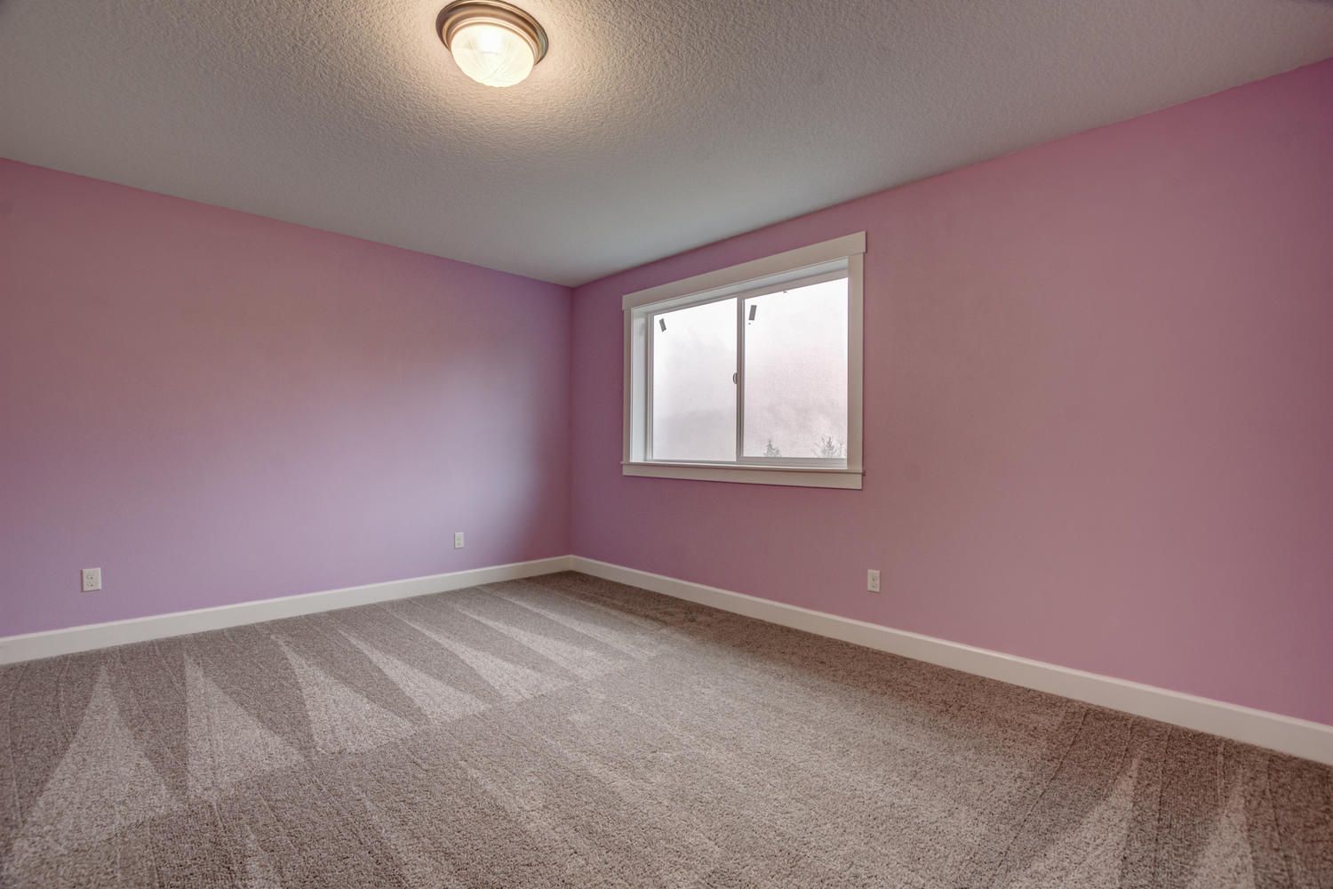 An empty bedroom with pink walls and a window.