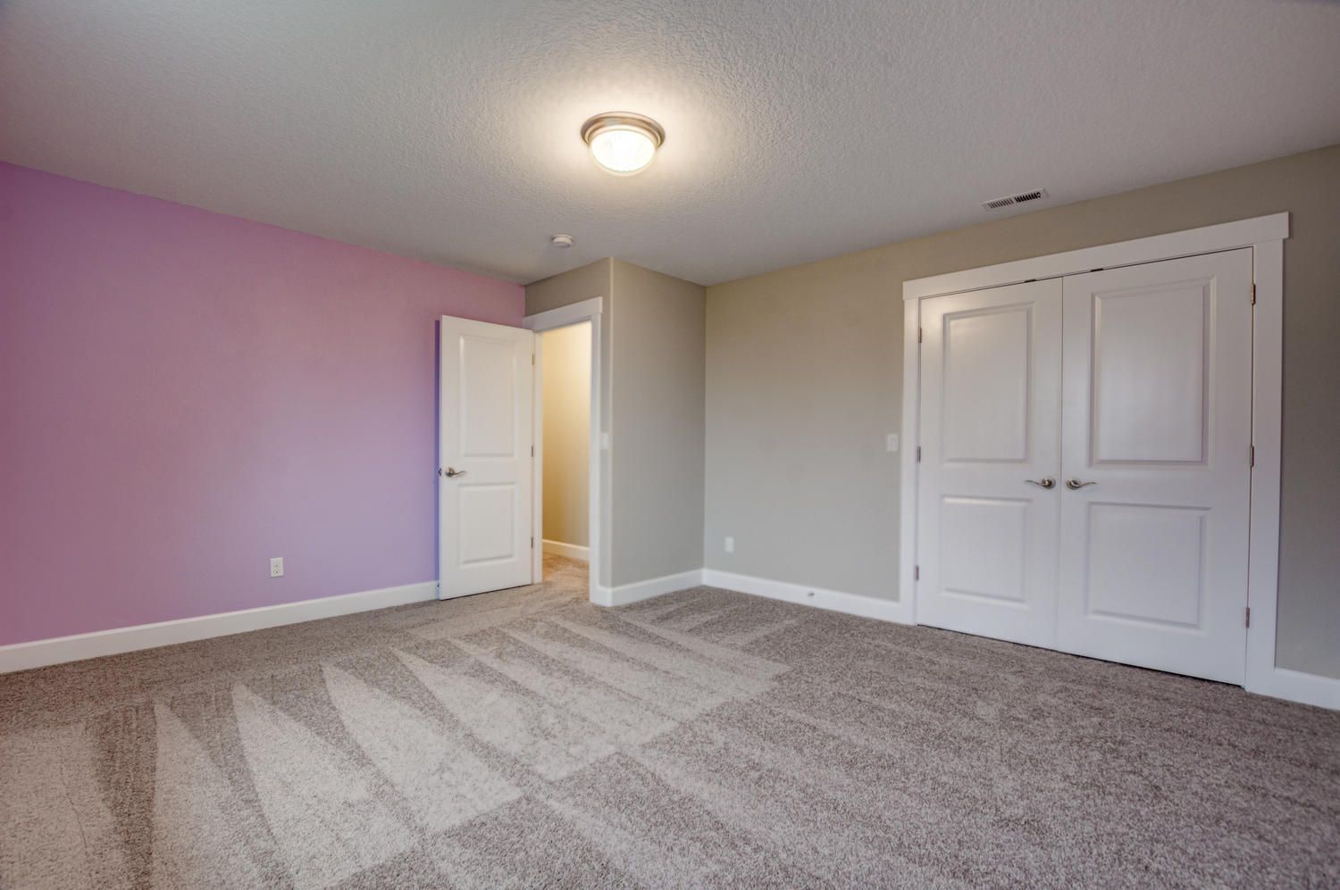 An empty bedroom with pink walls and a carpeted floor.