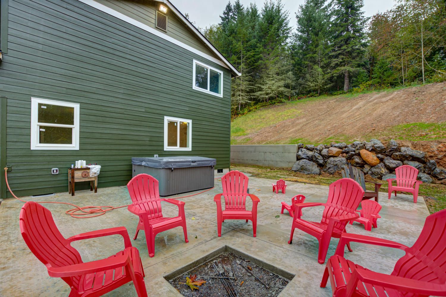A patio with red chairs and a fire pit in front of a house.