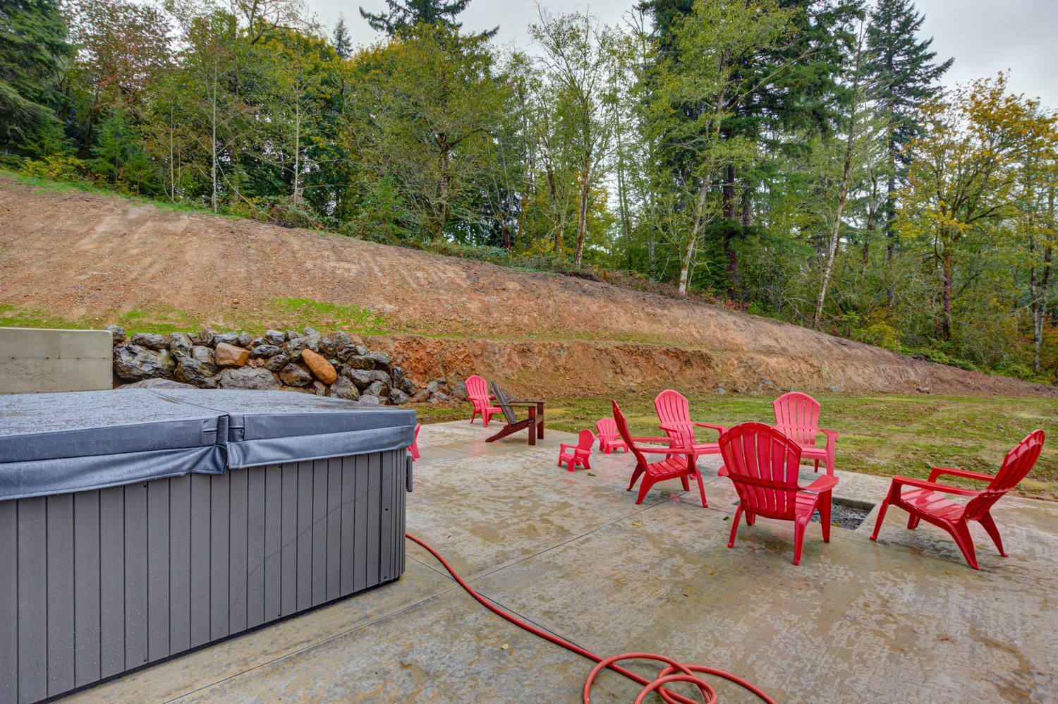 A hot tub is sitting next to a patio with red chairs and a hose.