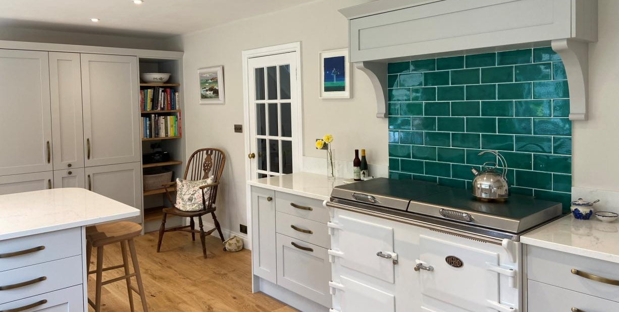 Light grey shaker kitchen with wood flooring and teal green metro tiled splashback