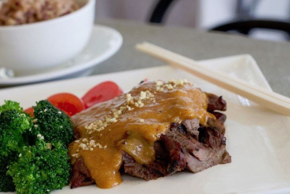 grilled hanger steak topped with peanut sauce with a side of vegetables.