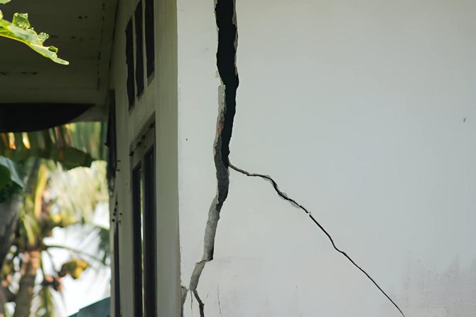 Cracked white wall with a large vertical crack beside a window and greenery outside