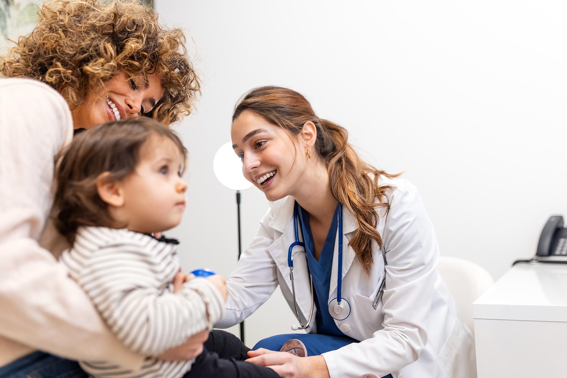 Doctor smiling and talking with a child and caregiver in a bright clinic exam room Doctor smiling and talking with a child and caregiver in a bright clinic exam room
