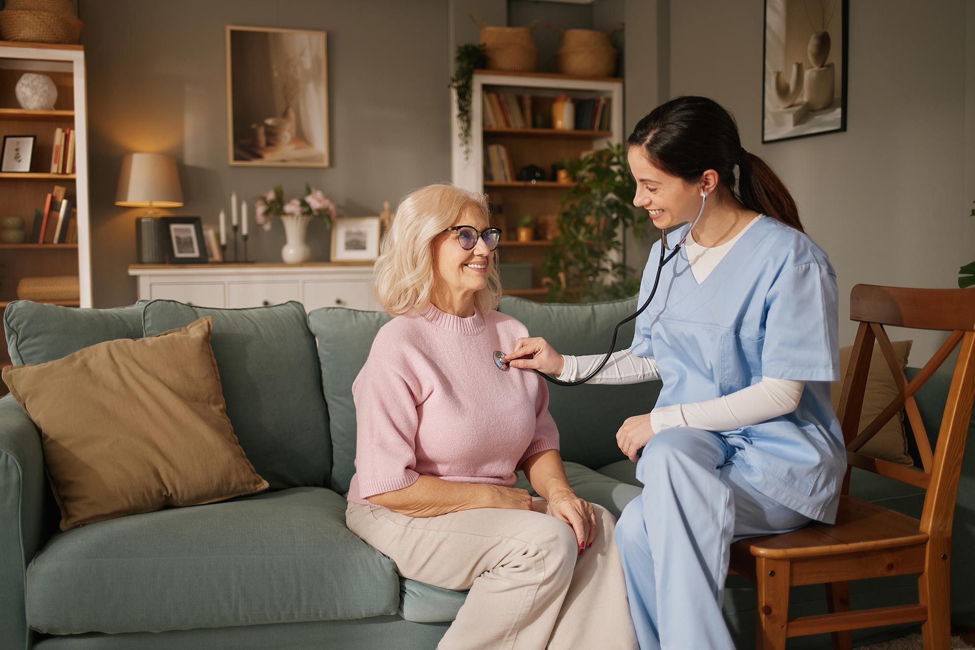 Nurse in blue scrubs checking an older woman’s chest on a couch in a cozy living room Nurse in blue scrubs checking an older woman’s chest on a couch in a cozy living room