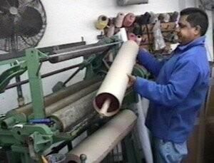 Worker handling a large white roll on a green industrial machine in a workshop