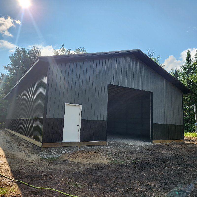 A newly built steel barn with grey vertical siding, a black wainscot, a white door, and a large open garage entrance.