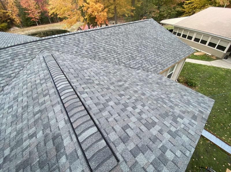 An elevated view of a residential roof covered in grey architectural shingles with a ridge vent.