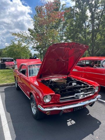 A red mustang with the hood up is parked in a parking lot.