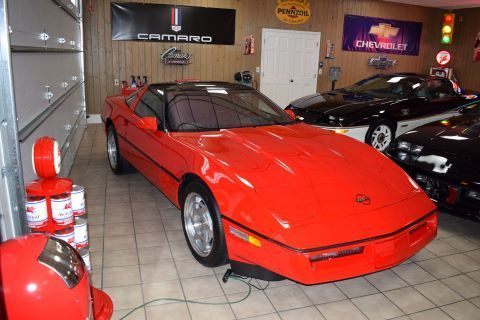 A red corvette is parked in a garage with other cars