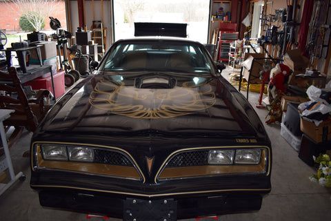 A black and gold pontiac trans am is parked in a garage.