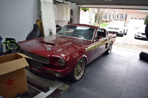 A red mustang is parked in a garage with the door open.