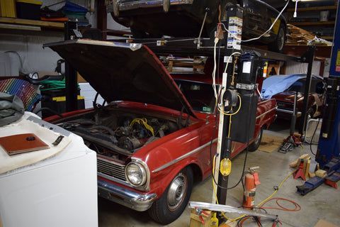 A red car is parked in a garage with the hood open.