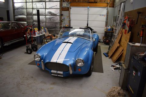 A blue sports car is parked in a garage next to a red car.