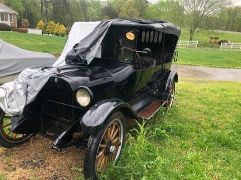 An old black car is parked in a grassy field.