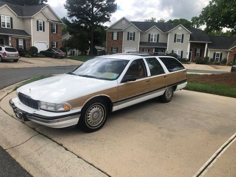 A white and brown car is parked in a driveway in front of a row of houses.