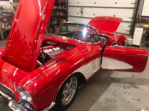 A red corvette with the hood up is parked in a garage.