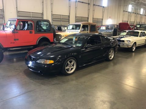 A black mustang is parked next to a red jeep in a garage.