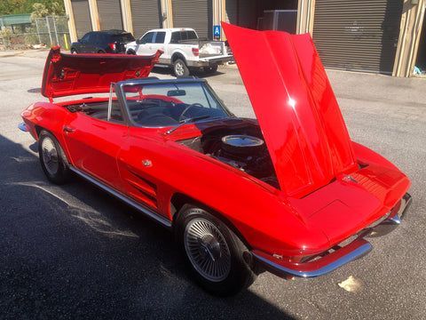 A red corvette convertible with the hood up is parked in a parking lot.