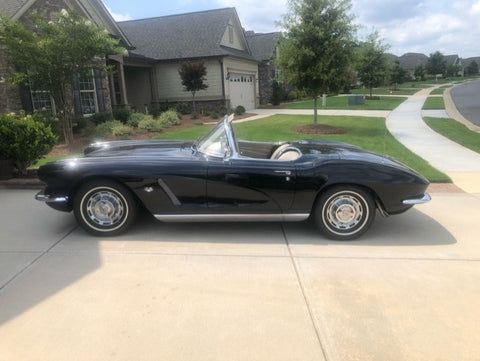 A black corvette convertible is parked in a driveway in front of a house.