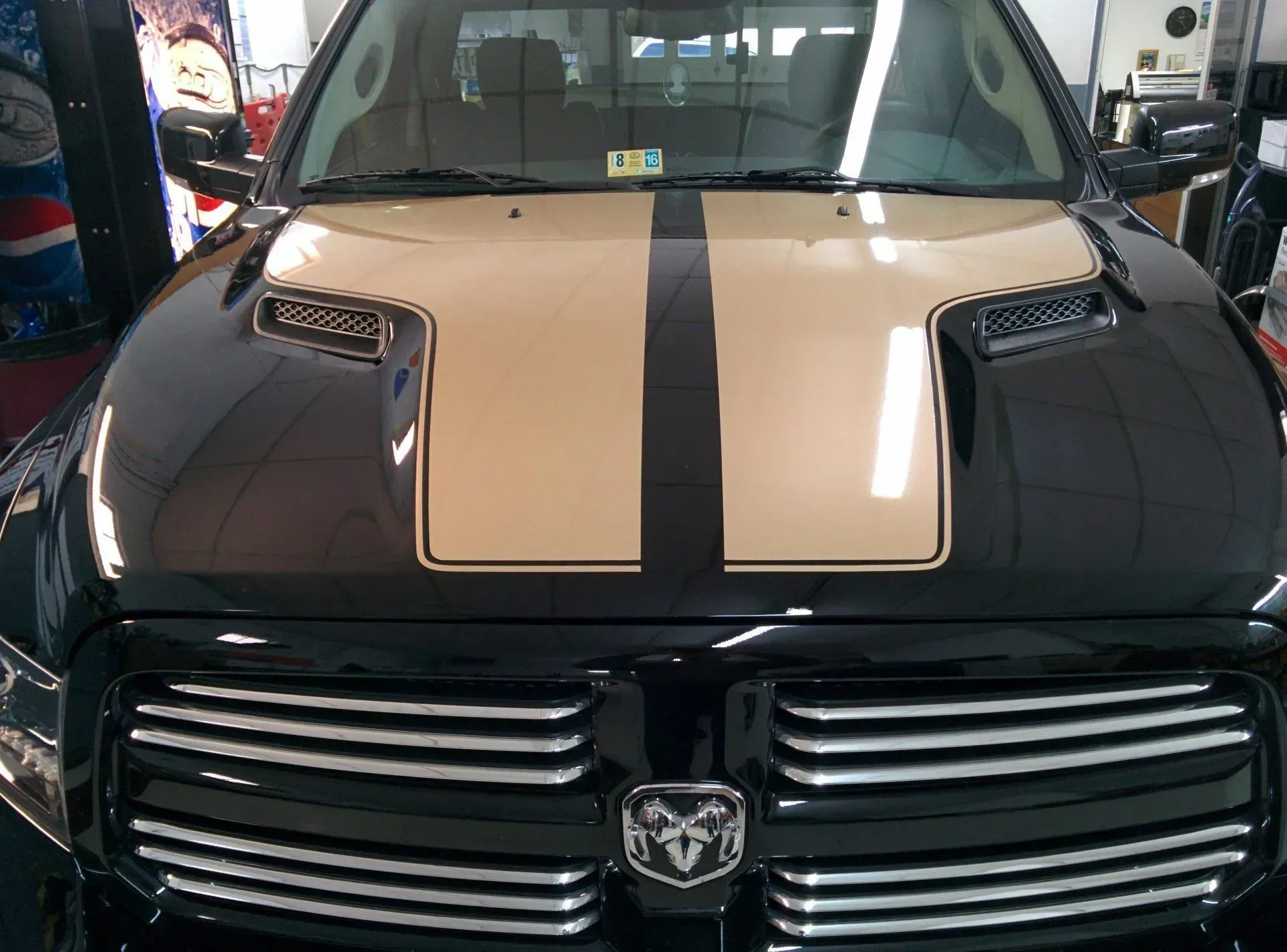 A black dodge ram with a tan stripe on the hood.
