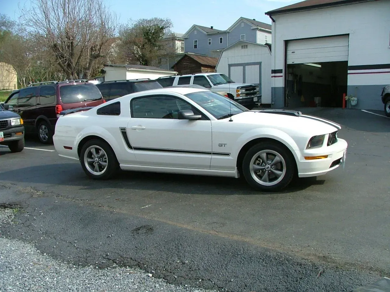 A white mustang is parked in front of a garage.
