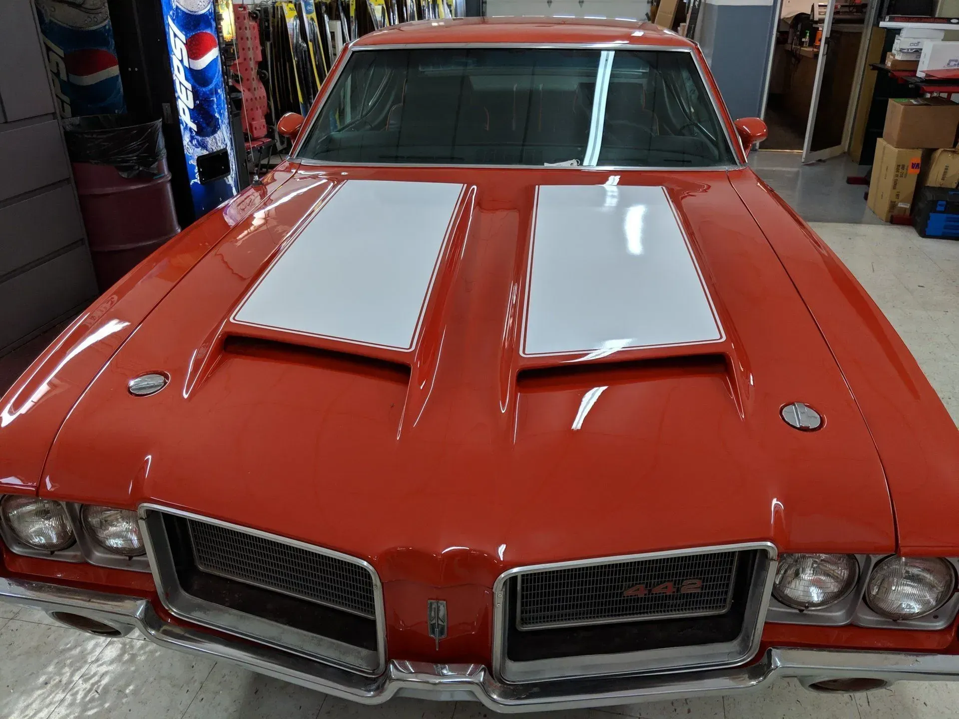 A red car with white stripes on the hood is parked in a garage.