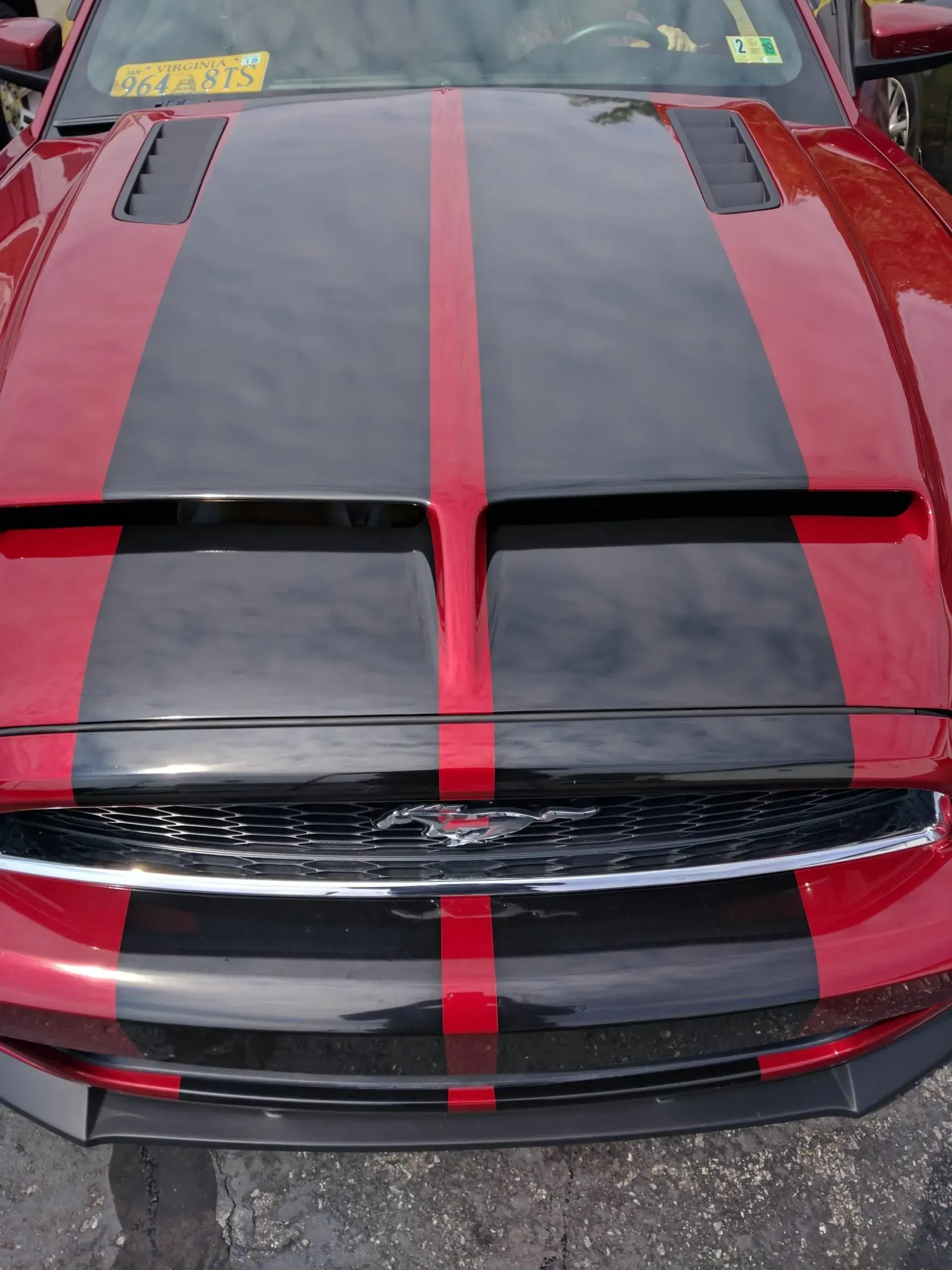 A red mustang with black stripes on the hood.