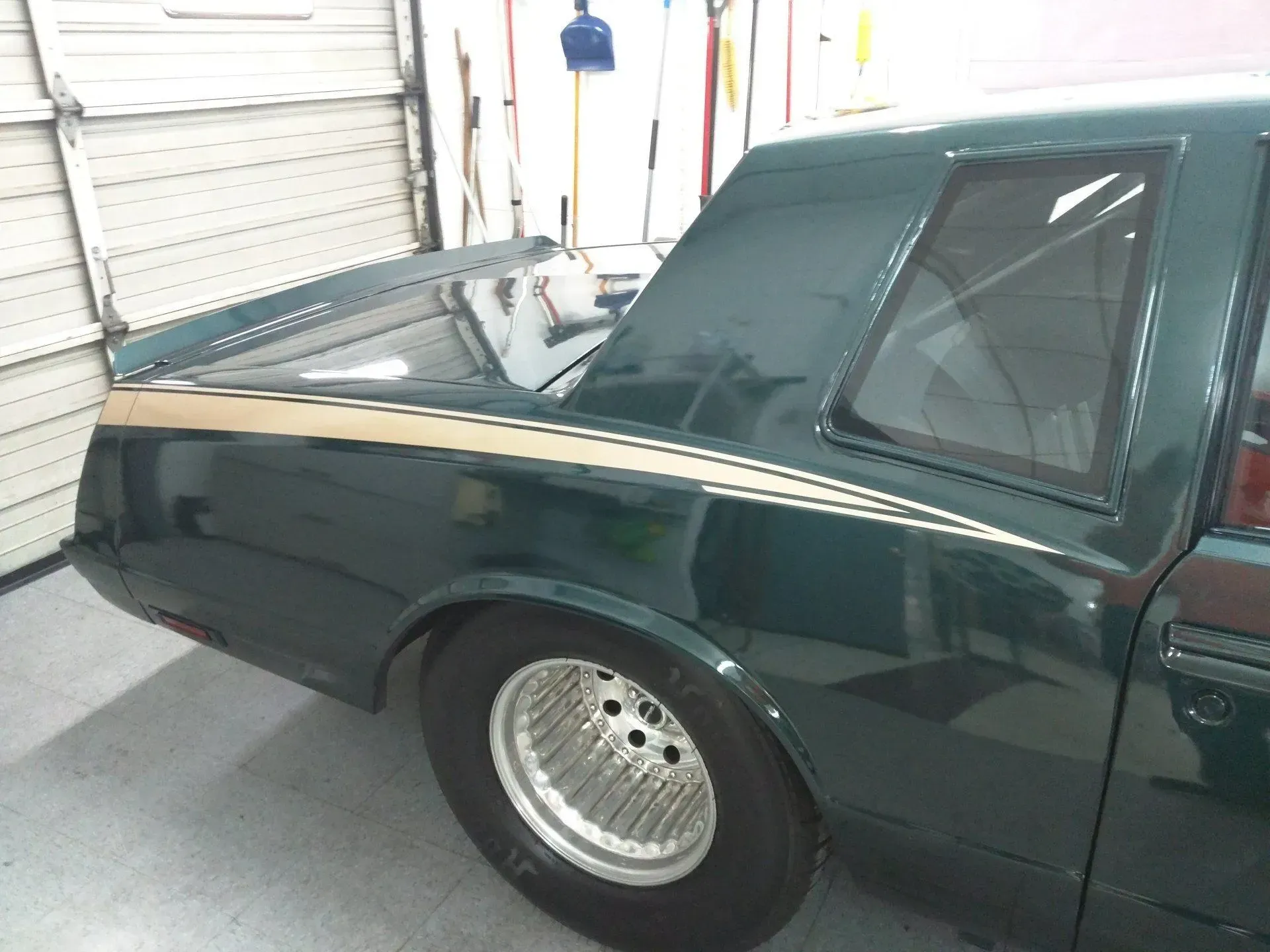 A green car is parked in a garage next to a garage door.