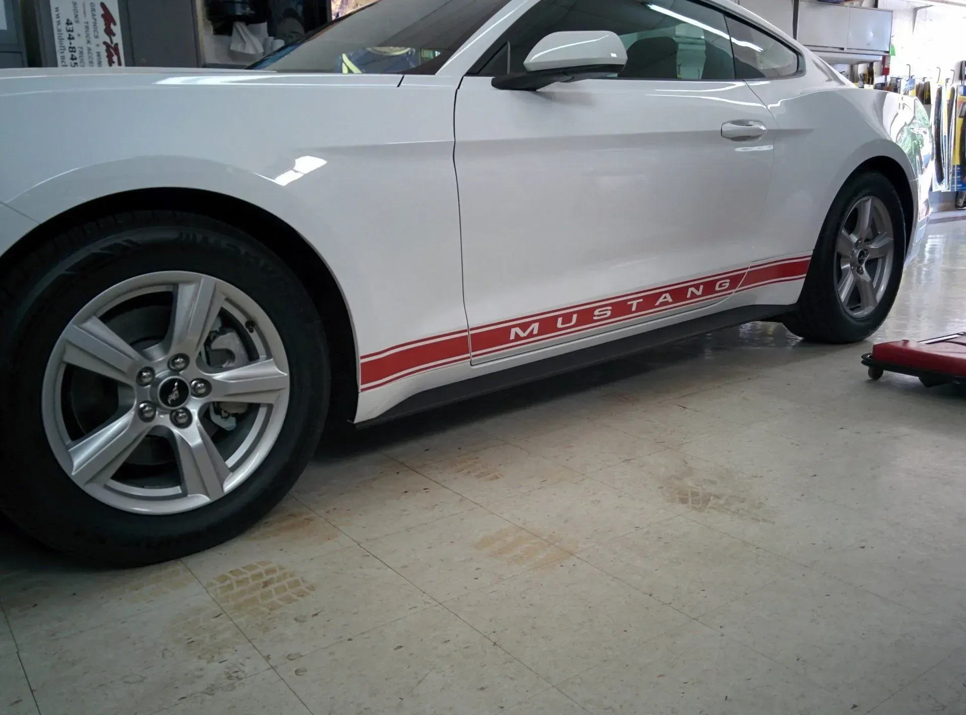 A white mustang with red stripes on the side is parked in a garage.